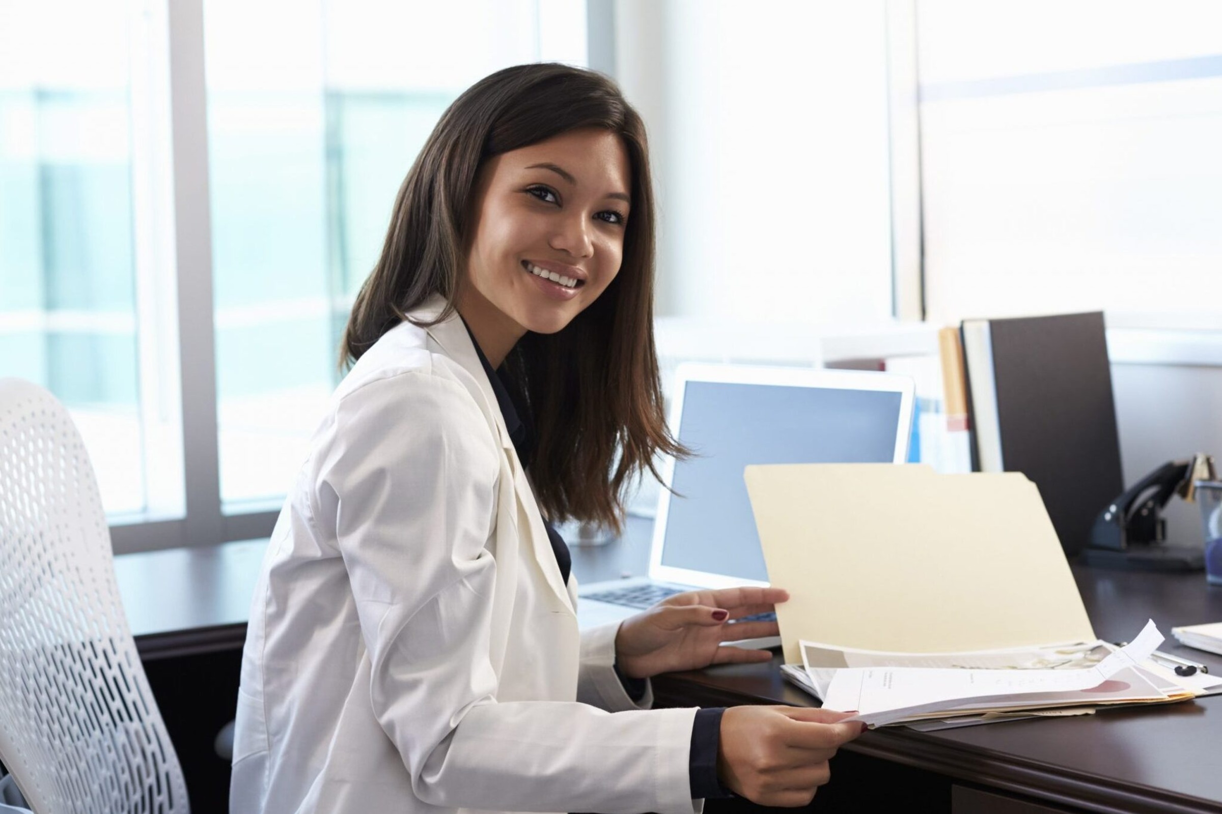 student in white lab coat sitting at a desk with file folder